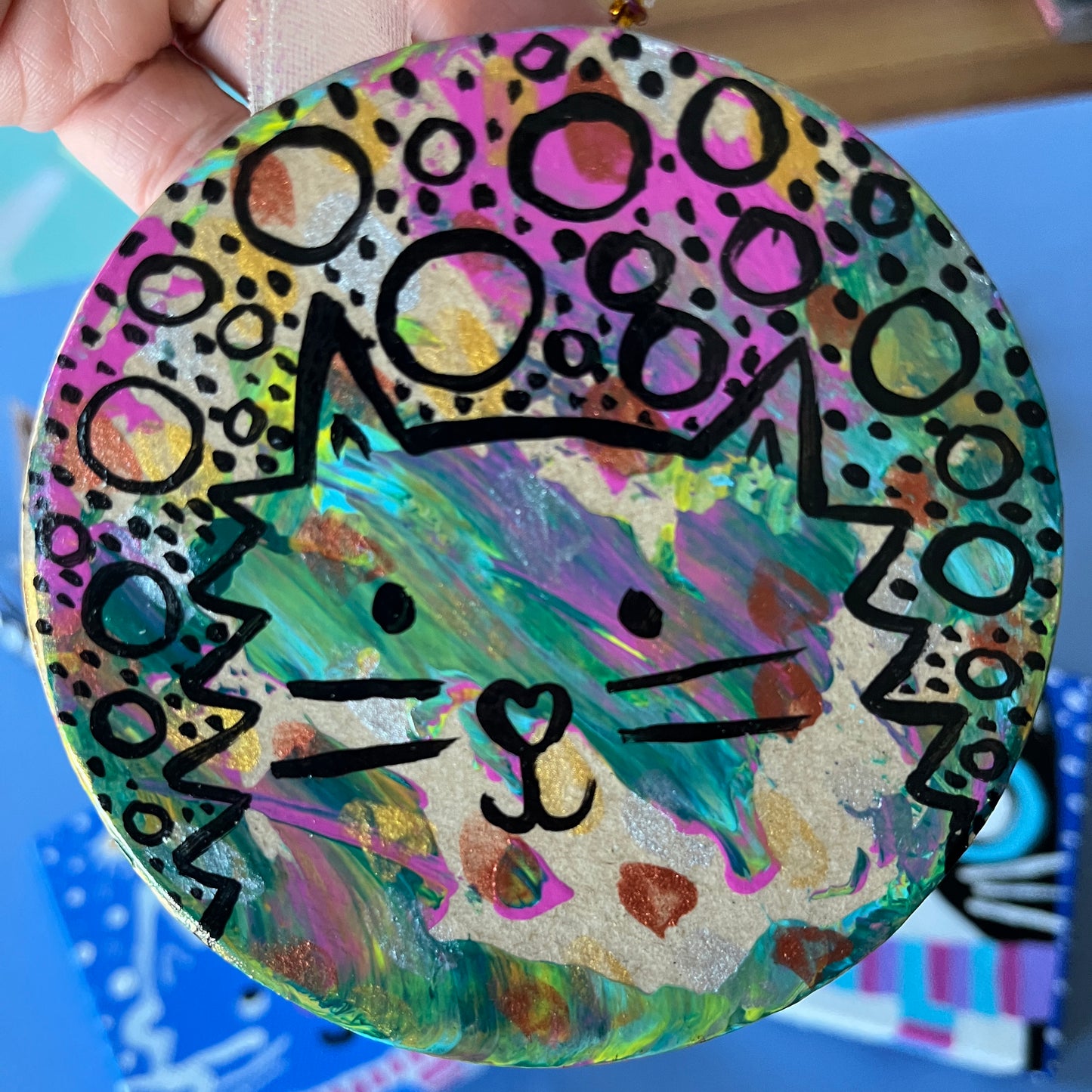 hand holding round ornament with splashes of color. black line art of a fluffy cat and circles and dots are on top of the colors